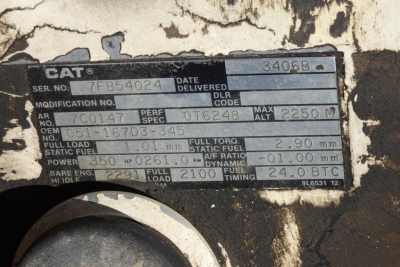Cat engine block data plate showing serial number 7FB54024, date delivered, engine specifications, fuel and torque values, and various codes on a weathered metal plate.
