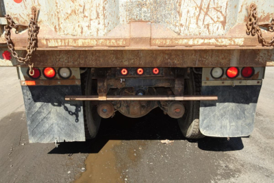 Dump truck rear showing rear lights and mud flaps, hitch and drive components under rusty dump bed.