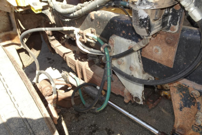 Engine bay view with wiring, hoses, and metal brackets in a Peterbilt 359 dump truck; visible components include cables, green hoses, and rusted metal surfaces.