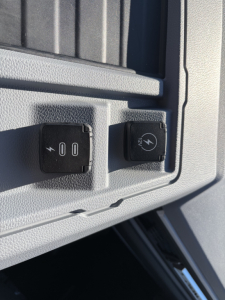 Truck dash area with two power/auxiliary controls and a 12V outlet diagram and a symbol; visible text includes '00' or power icon on switch and a 12V plug icon.