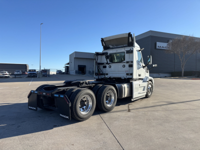 Truck showing a white Mack PR64T conventional day cab chassis with multiple axles, detached cab tilt, and rear view in a dealership lot.