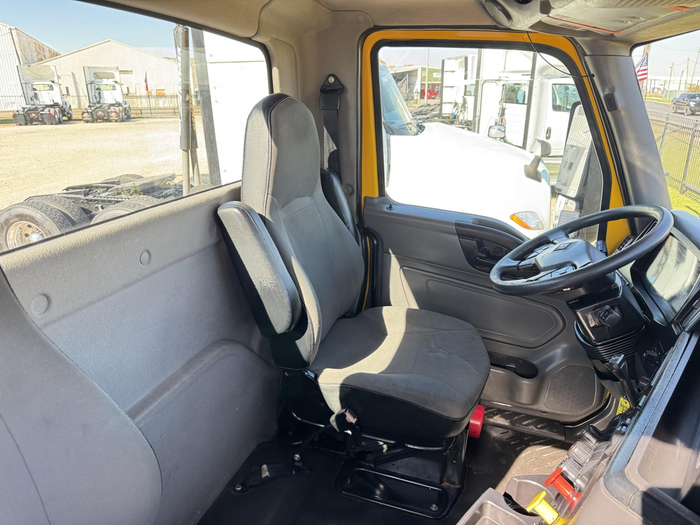 Truck cab interior of a 2019 International LT daycab showing driver seat, steering wheel, and dashboard from the passenger side window.