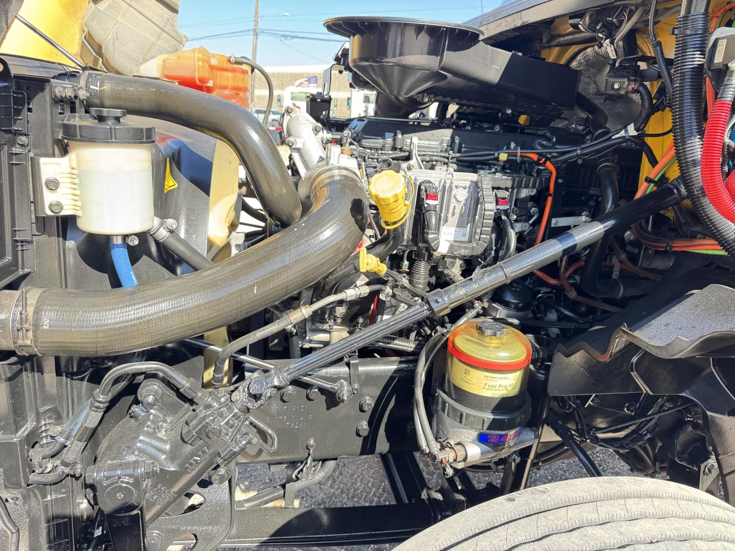 Engine bay of 2019 International LT showing coolant reservoir, hoses, yellow oil filter cap, and multiple components.