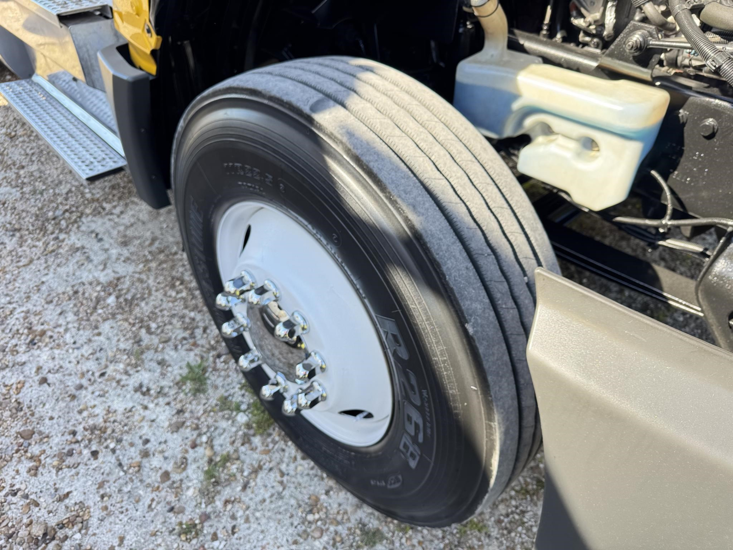 Front axle area of a 2019 International LT conventional daycab showing a single front tire mounted on white wheel with lug nuts; engine bay and coolant reservoir visible.