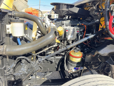 Engine bay of 2019 International LT showing coolant reservoir, hoses, yellow oil filter cap, and multiple components.