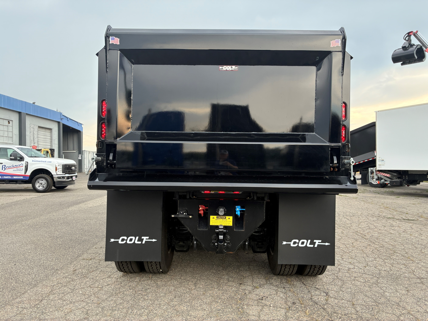 Truck bed of 2026 Mack PI64 dump truck showing rear view with black dump body and dual rear wheels, safety decals, and coupler area.