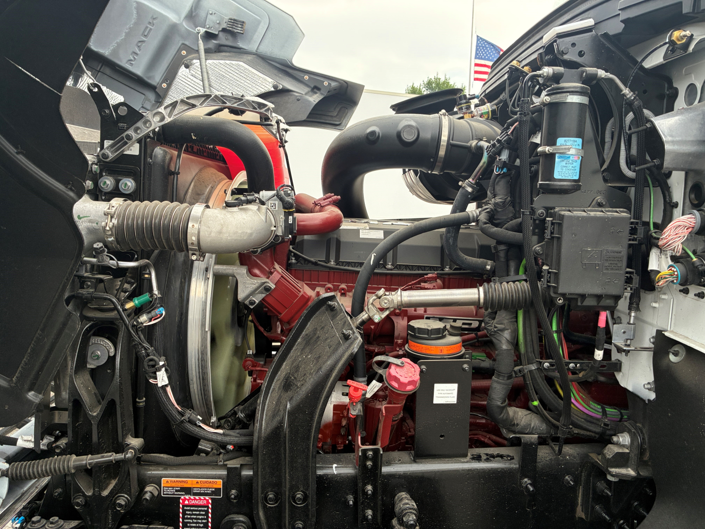 Engine bay of a 2026 Mack PI64 dump truck showing red engine, intercooler piping, hoses, wiring harness, and air intake components.