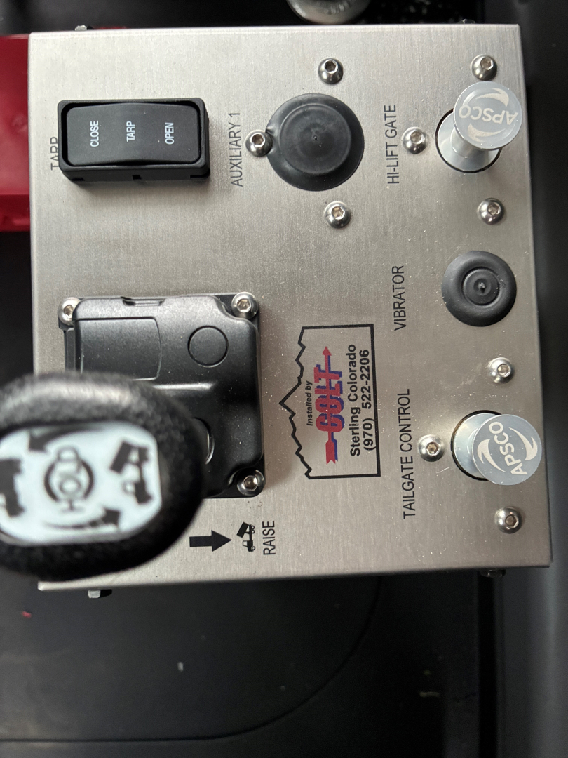 Mack PI64 control panel with switches and labels including AUXILIARY, TILT/TAILGATE, VIBRATOR, PTO, and a circular knob showing ASCO and APD logos, with wiring and a lever in view.