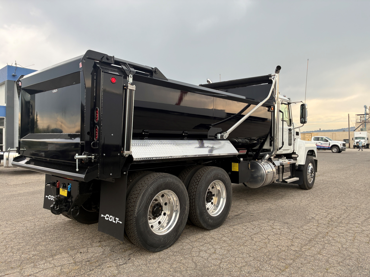 Dump truck configuration showing rear dump bed and dual rear axles on a Mack PI64 chassis with black dump body, chrome steps, and aluminum toolbox.