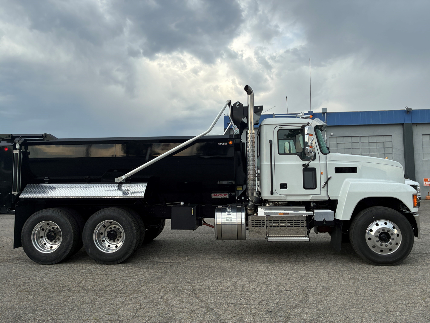 Mack PI64 dump truck side view showing long black dump bed and white cab, chrome exhaust stack, and steps.