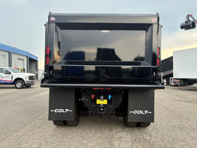 Truck bed of 2026 Mack PI64 dump truck showing rear view with black dump body and dual rear wheels, safety decals, and coupler area.