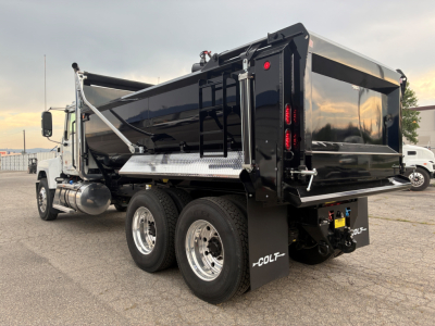 Truck rear/right side view showing a black dump body on a Mack PI64 chassis with dual rear axles, side step, and COLT branding on mud flaps; no visible text labels or numbers on body.