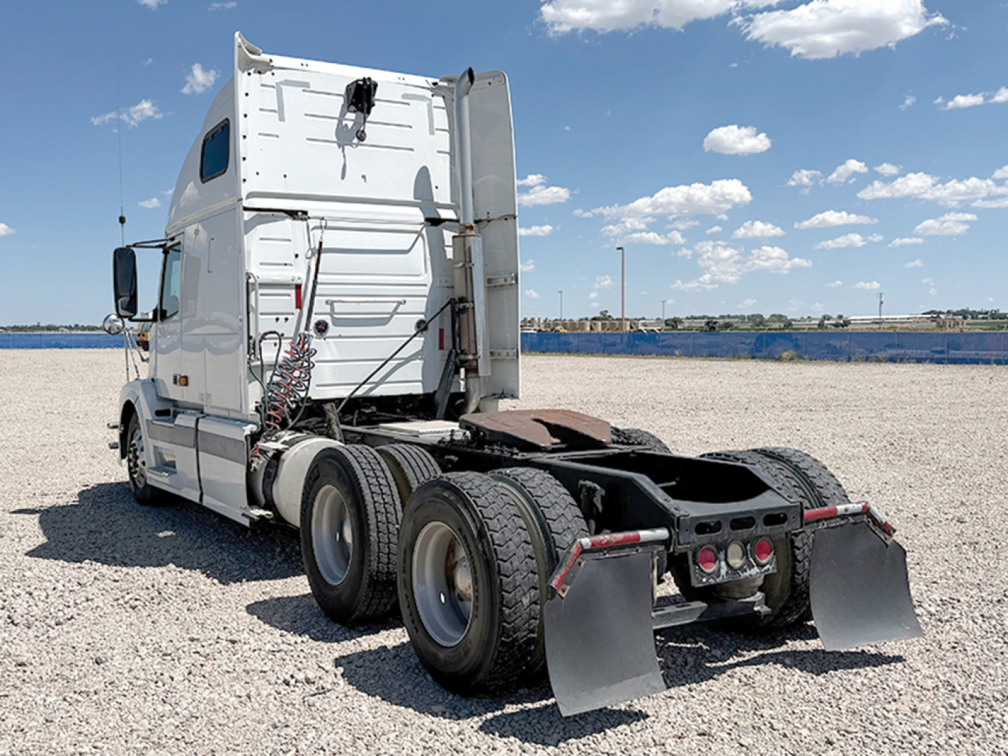 Side rear view of a white Volvo VNL 670 tractor truck with dual rear axles and fifth wheel, parked on gravel. Visible features include back cab, exhaust, and mud flaps.