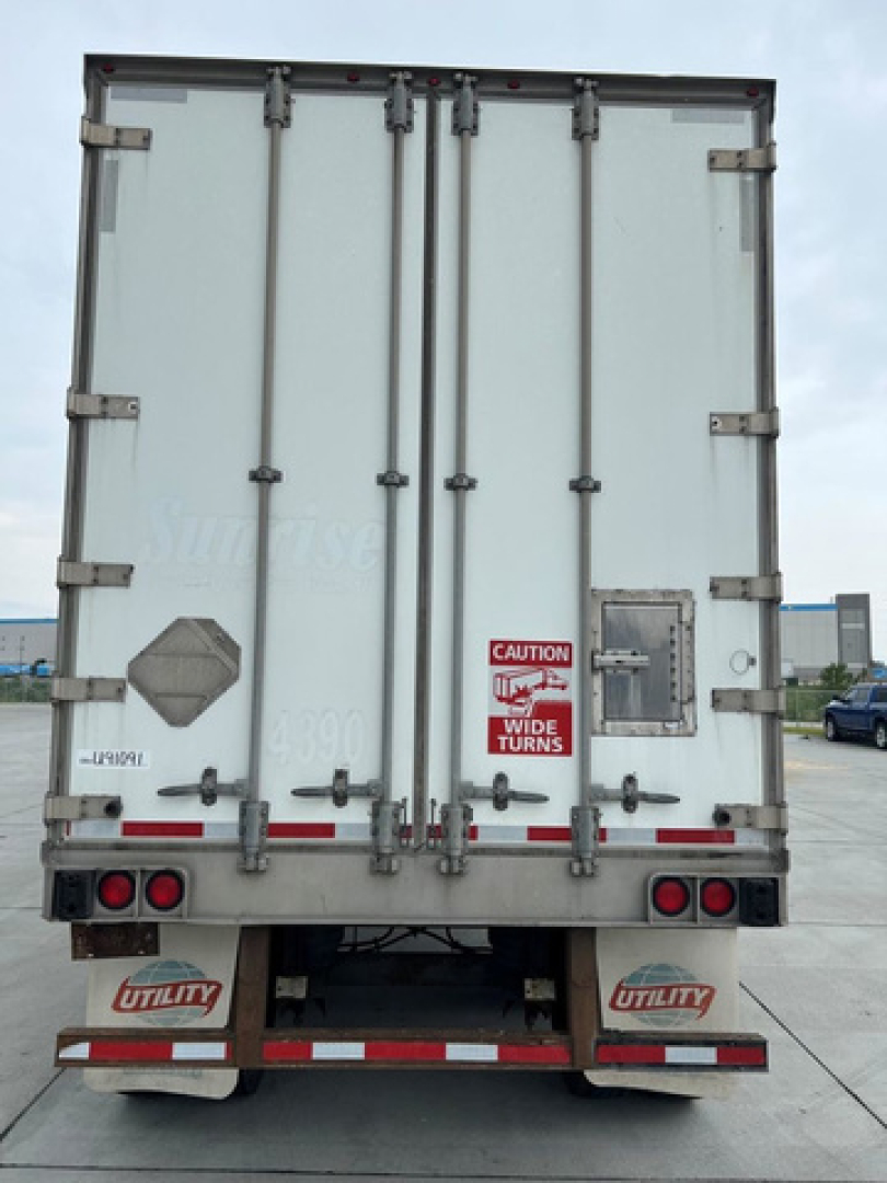 Trailer rear of a white utility van with doors and latches, CAUTION wide turns sticker, lights, and utility branding on mudflaps.