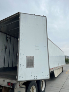Trailer rear door opening showing interior of box truck trailer with loading area and wheel wells visible.