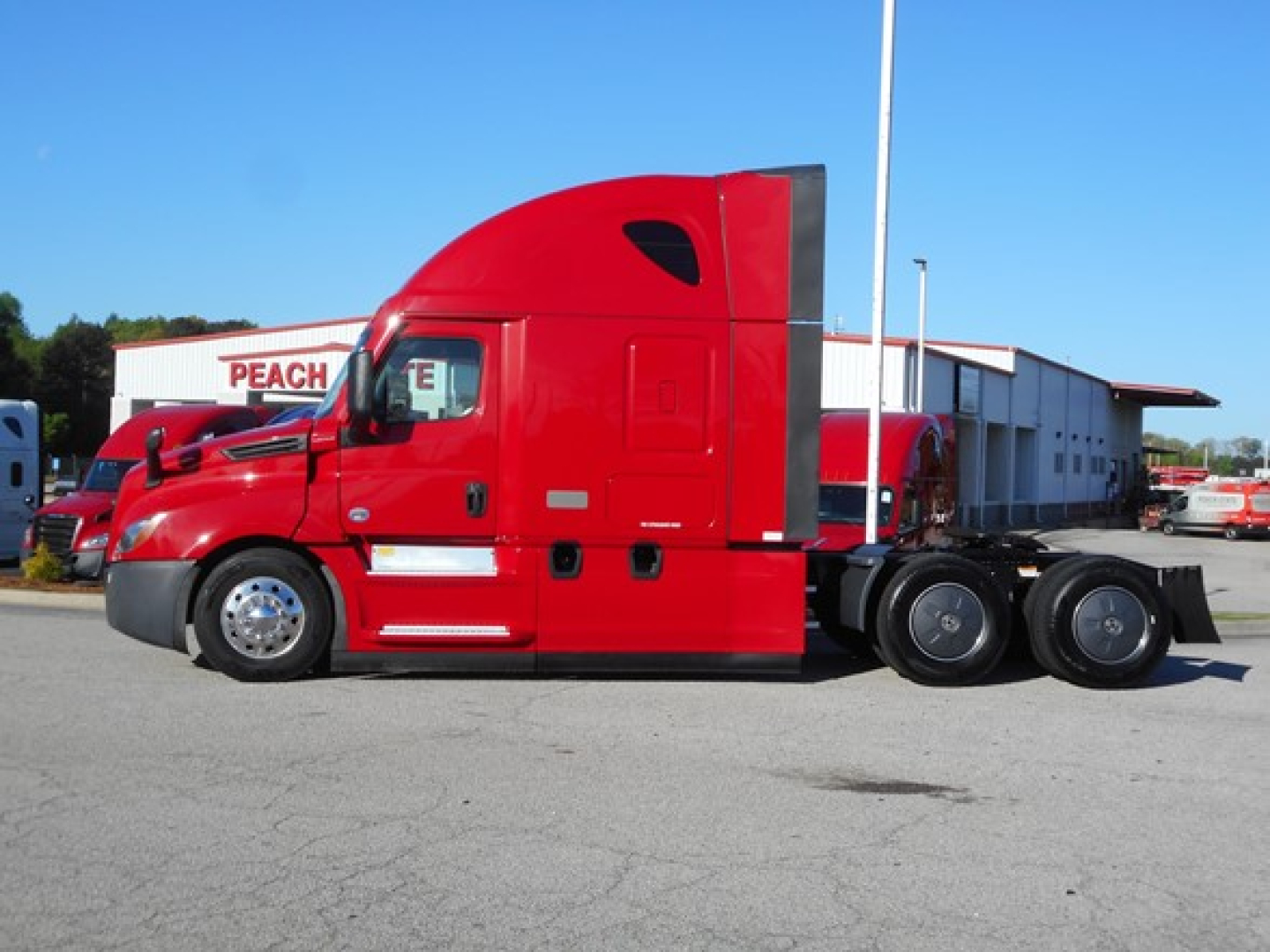 Freightliner Cascadia 126 sleeper cab side view showing bright red exterior and three-axle configuration with cargo area at rear.