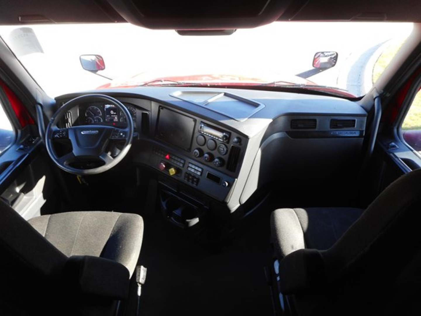 Cab interior of a Freightliner Cascadia truck showing steering wheel, dashboard with multiple gauges, center console, and seats.