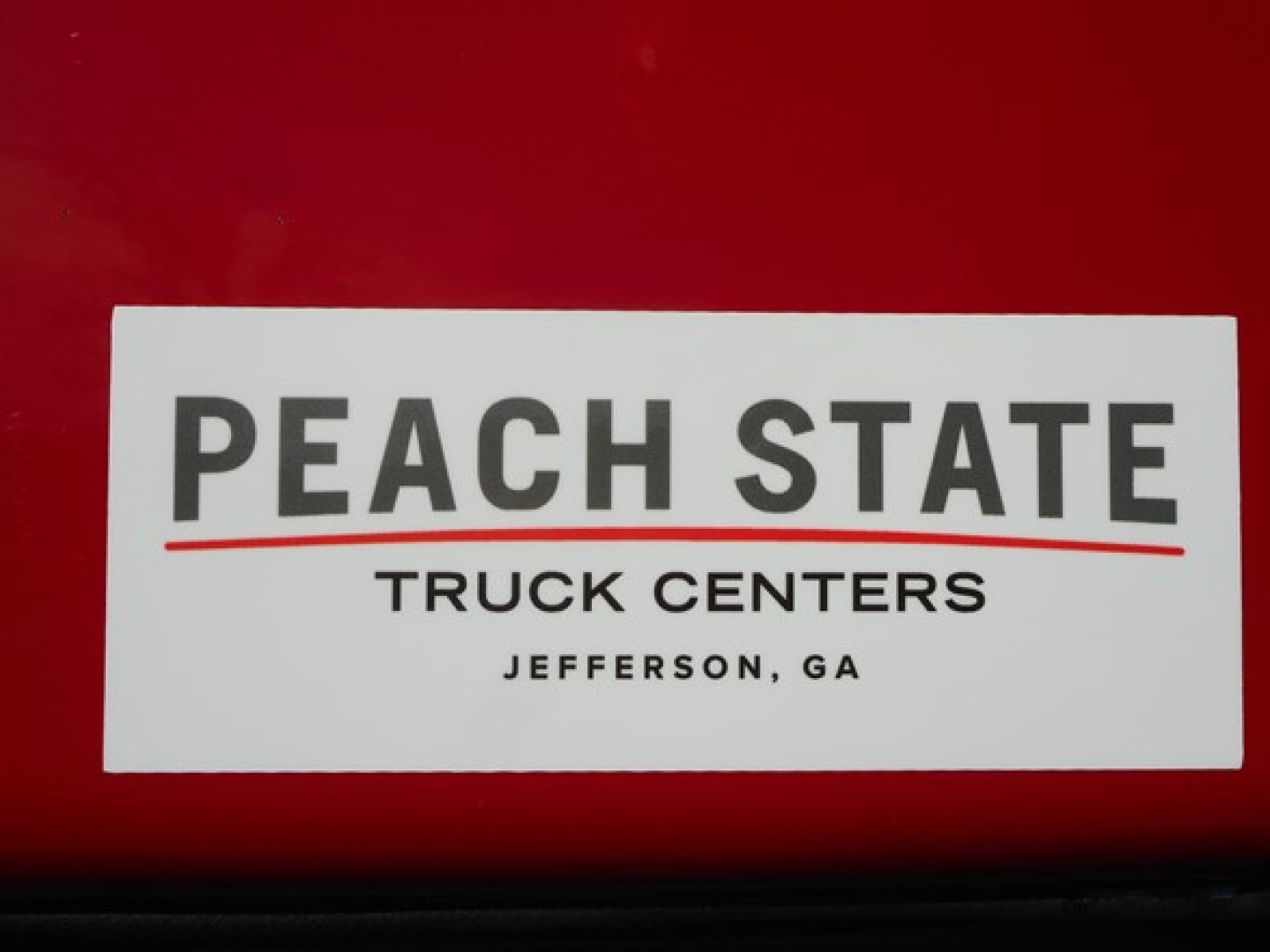Peach State Truck Centers sticker on red surface showing PEACH STATE TRUCK CENTERS JEFFERSON, GA with a red underline under PEACH STATE.