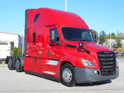 Conventional sleeper truck cab of a red 2023 Freightliner Cascadia 126 shown in a parking lot, front-left view; visible features include large grille, dual rear axles, side mirrors, and sleeper cab window.