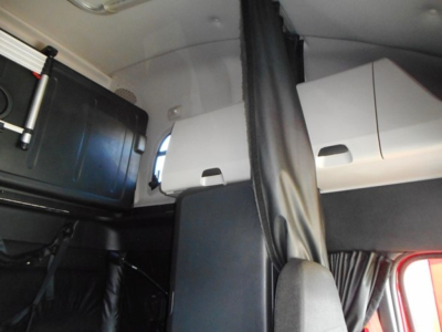 Cab interior of a Freightliner Cascadia sleeper showing storage compartments and bunk area.