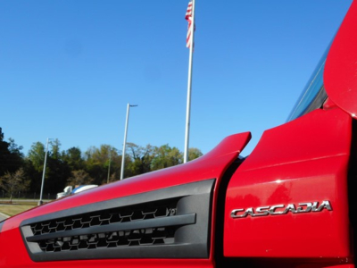 Close-up of a red Freightliner Cascadia truck showing the 'CASCADA' badge on the side and part of the black grille.