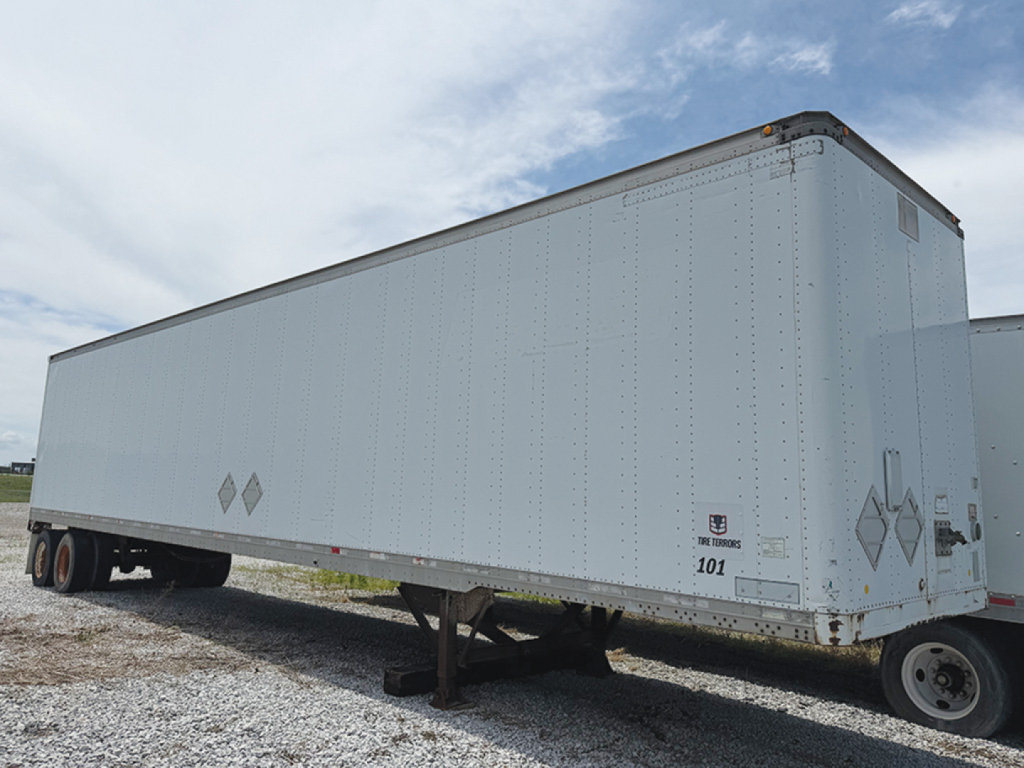 Aluminum cargo trailer trailer side view showing riveted silver surface with diamond hazard placards and loading tires under.