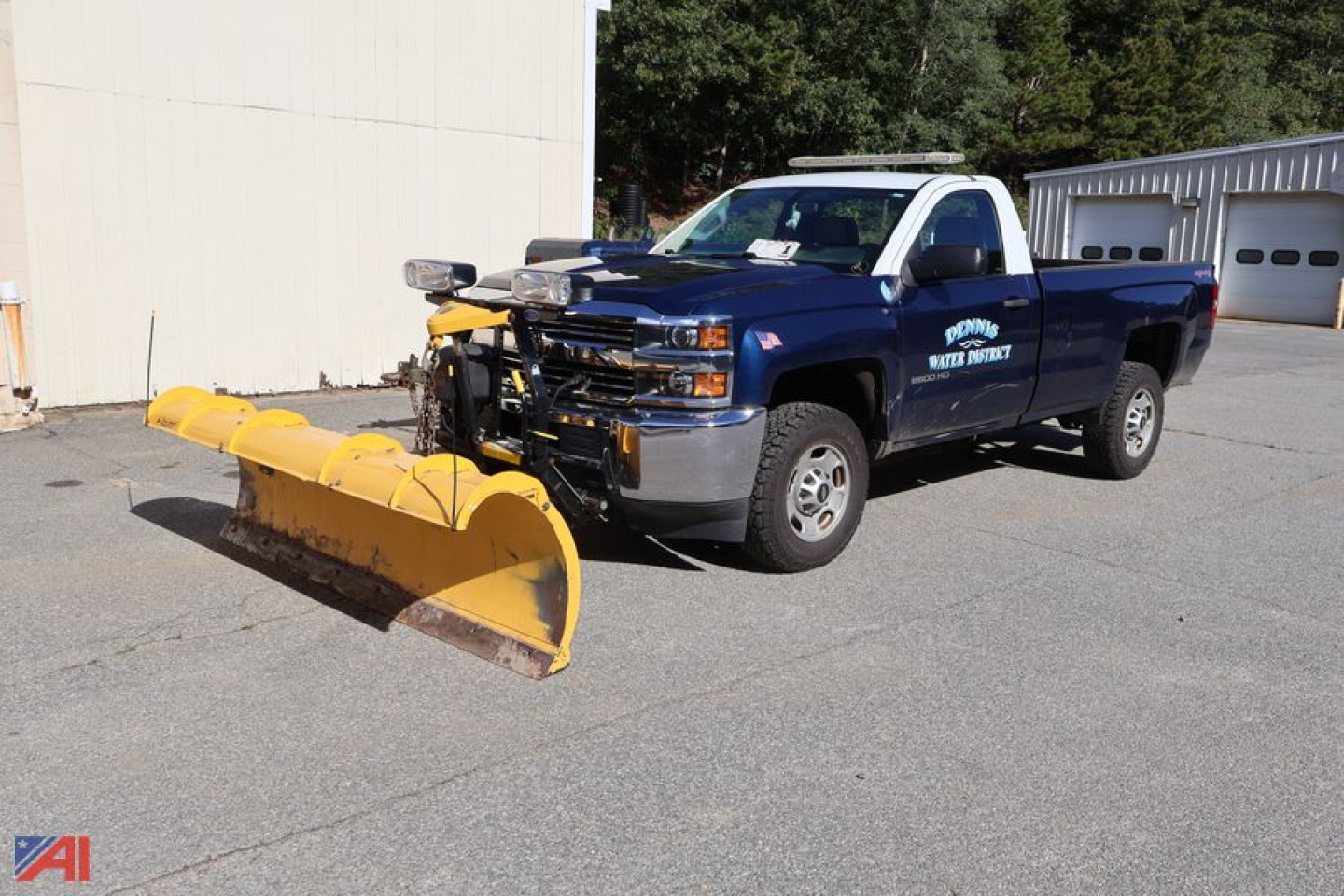 Chevrolet Silverado 2500 pickup with a large yellow snow plow attached, blue body, front grille and headlights visible, dealership or utility markings on door.
