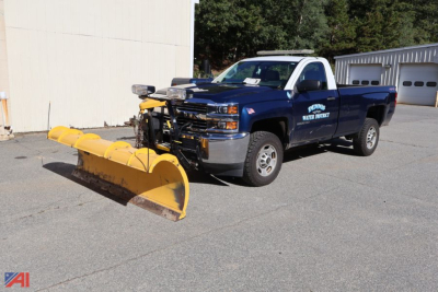 Chevrolet Silverado 2500 pickup with a large yellow snow plow attached, blue body, front grille and headlights visible, dealership or utility markings on door.