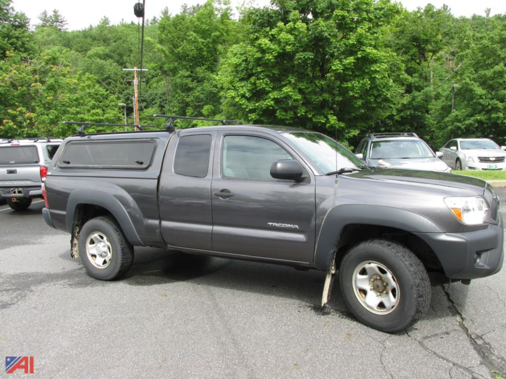 Toyota Tacoma pickup truck with cap, gray exterior, 4-door crew cab, positioned in a parking lot.