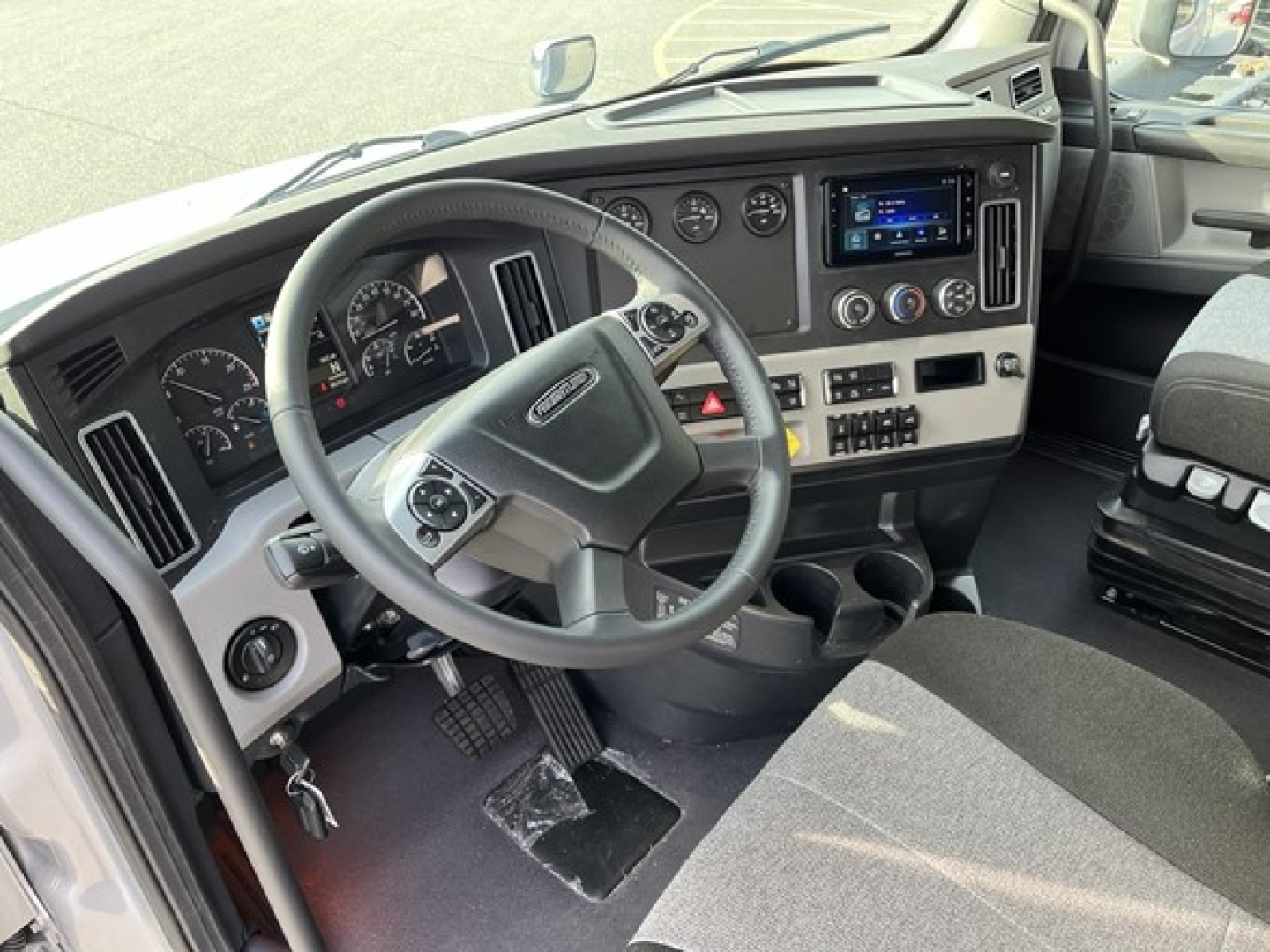 Truck cab interior showing steering wheel, dashboard, gauges, and center console of a 2026 Freightliner Cascadia 126 with a touchscreen infotainment and multiple switches.