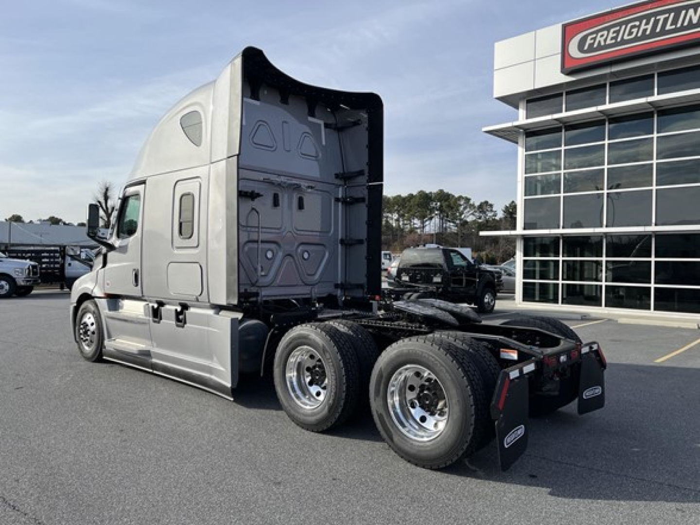 Freightliner Cascadia 126 tractor in a dealership lot, left-rear view showing sleeper cab, chassis, and dual rear axles with black mud flaps.