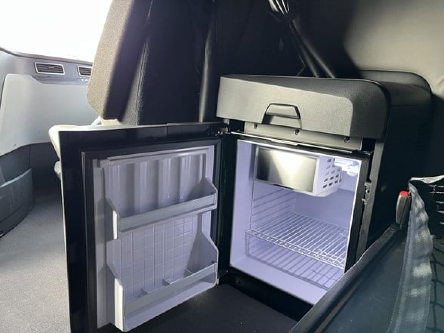Freightliner Cascadia truck cab interior showing a small refrigerator with open door and empty shelves inside.