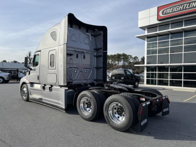 Freightliner Cascadia 126 tractor in a dealership lot, left-rear view showing sleeper cab, chassis, and dual rear axles with black mud flaps.