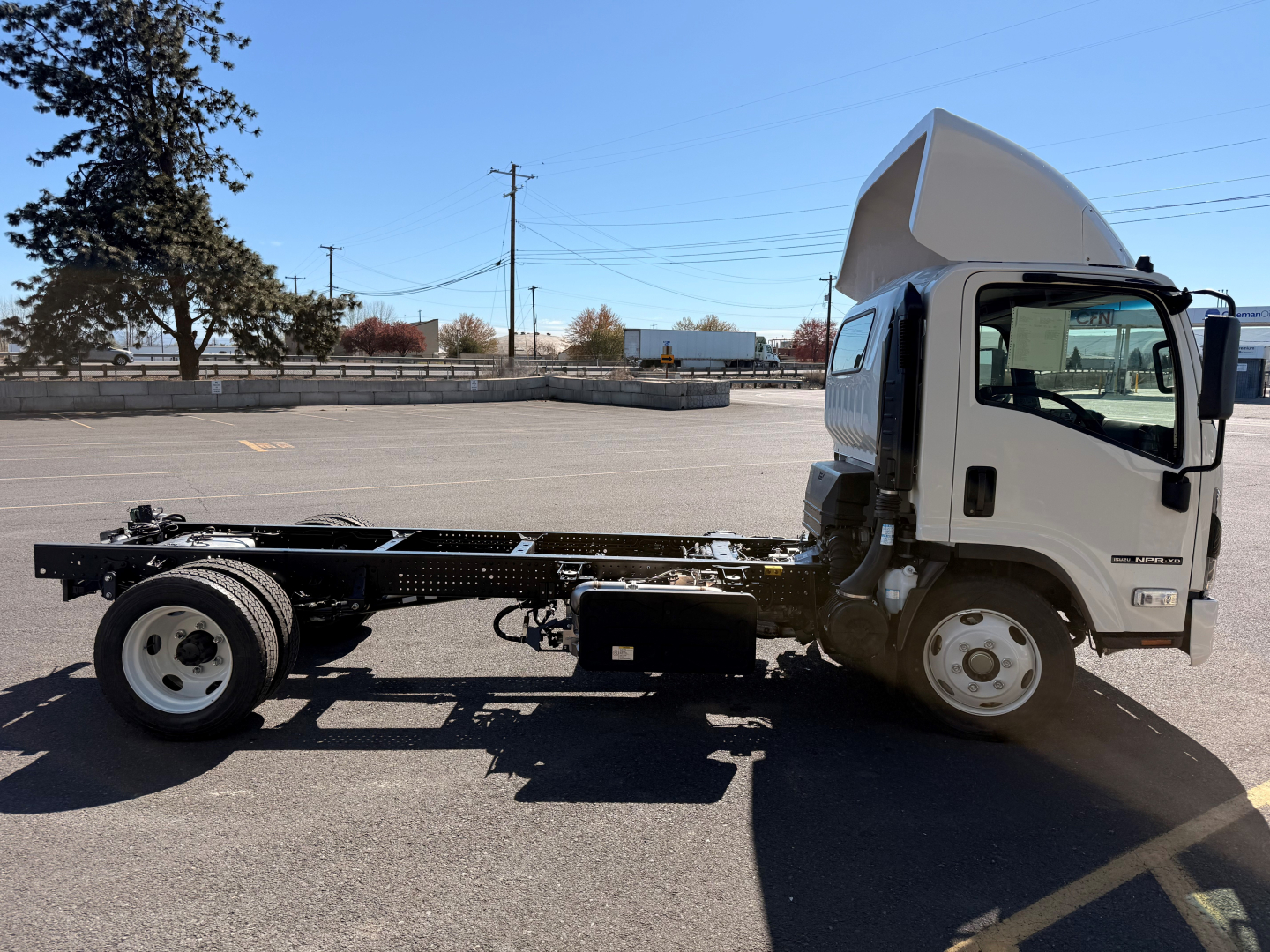Isuzu NPRXD cab and chassis side view showing empty chassis with raised cab and front wheel, no body bed attached.