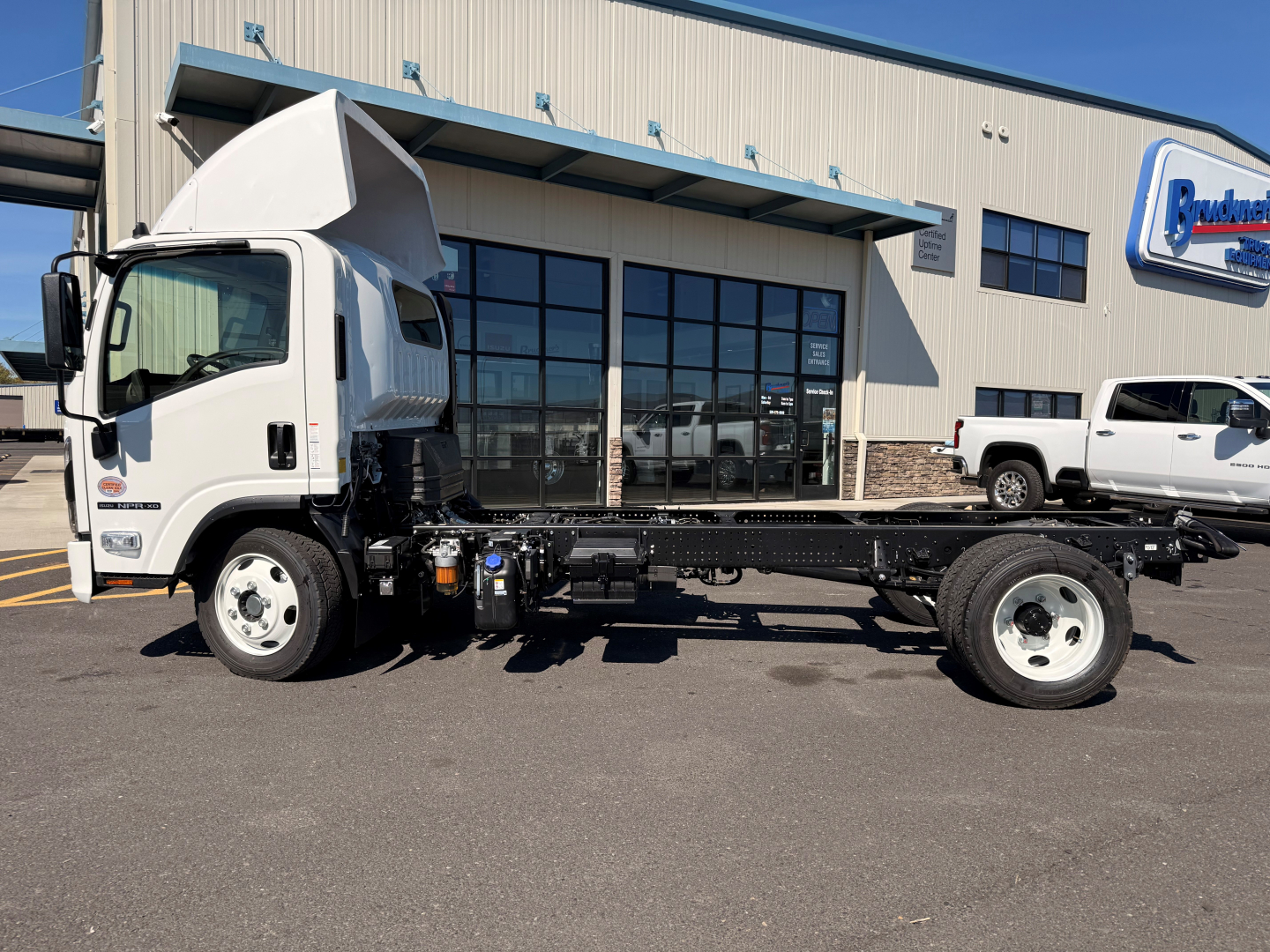 Isuzu NPRXD cab chassis truck in a dealership lot with a raised cab, showing wheelbase and chassis frame.