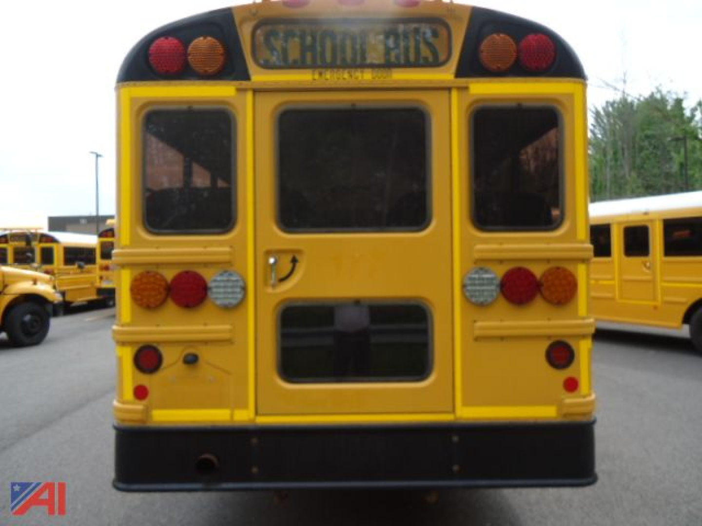 Back view of a yellow IC Corporation CE Series school bus with red and amber lights, rear window, and SCHOOL BUS signage above; surrounding buses visible.