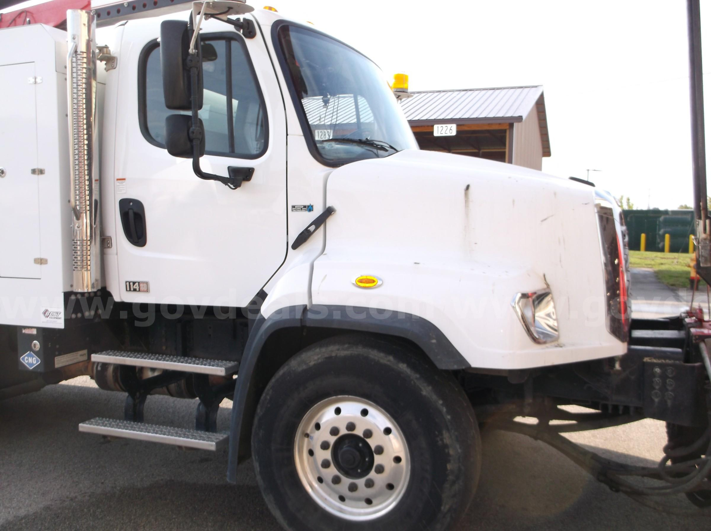 Freightliner 114SD vacuum truck front-left view showing cab and white body with side step.