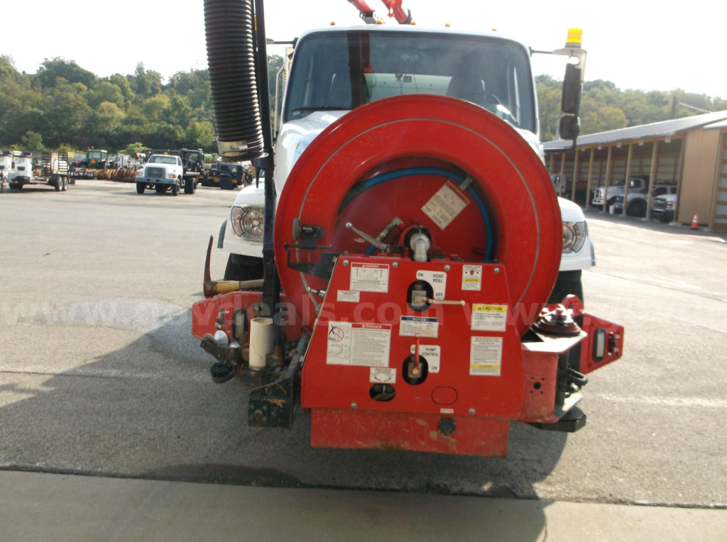 Front view of a Freightliner 114SD vacuum truck showing a red hose reel and control panel mounted on the front bumper area.