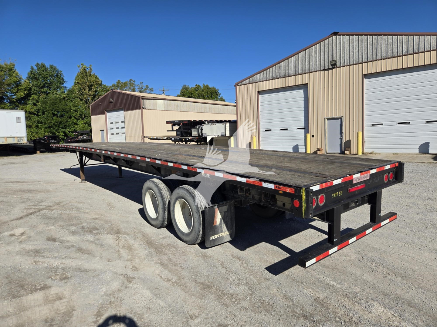 Flatbed trailer showing a Fontaine steel flatbed with triple axle and dual-tandem wheels, rear ramps, and safety reflectors.