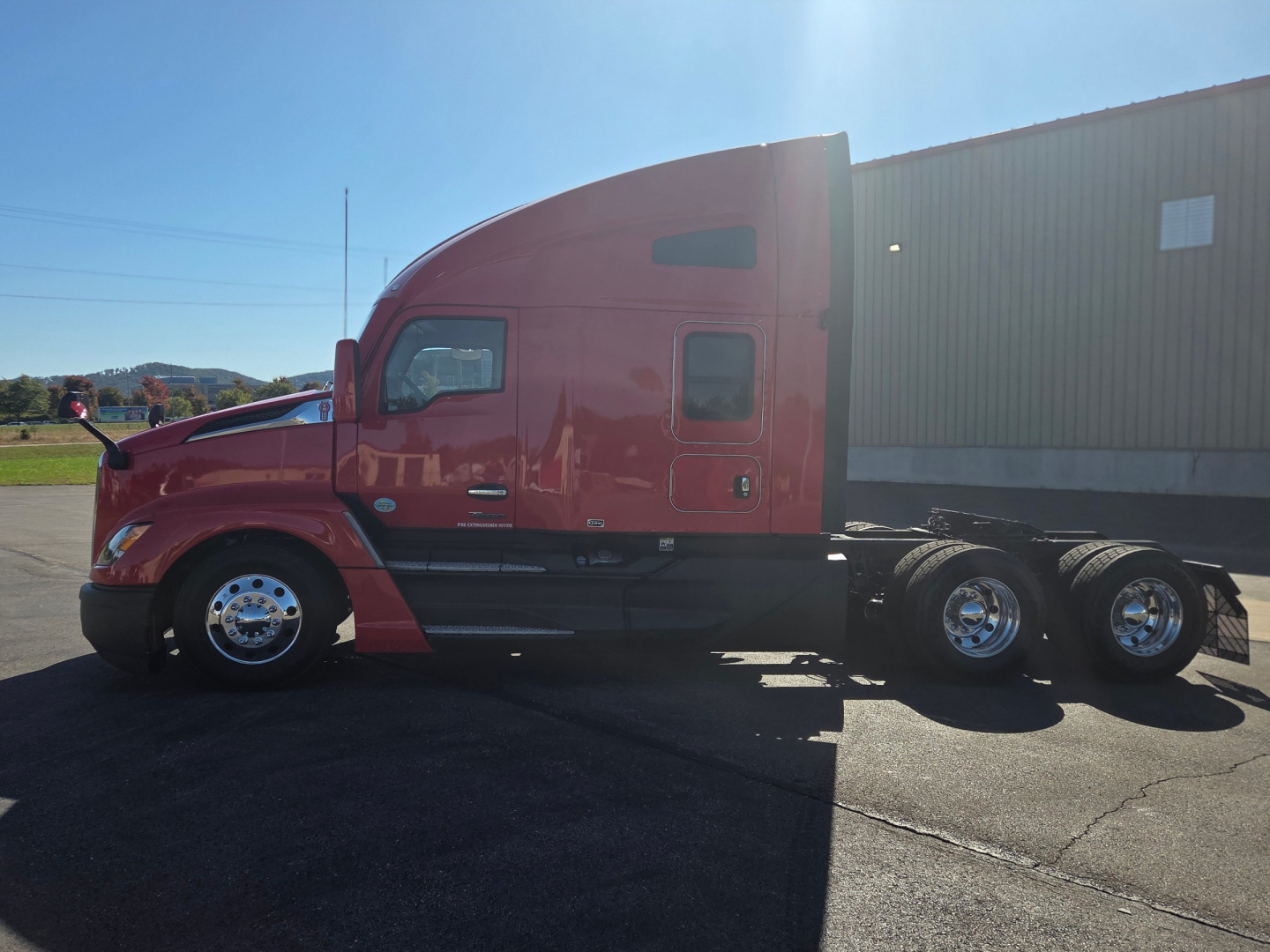 Kenworth T680 conventional sleeper truck side view showing red cab and tandem rear axles with chrome wheels.