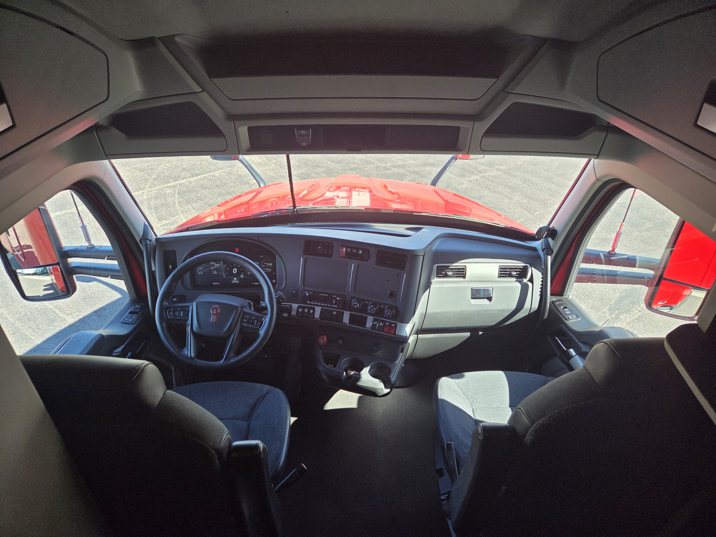 Kenworth T680 truck cabin interior center dashboard with steering wheel, multiple controls, and large windshield view.