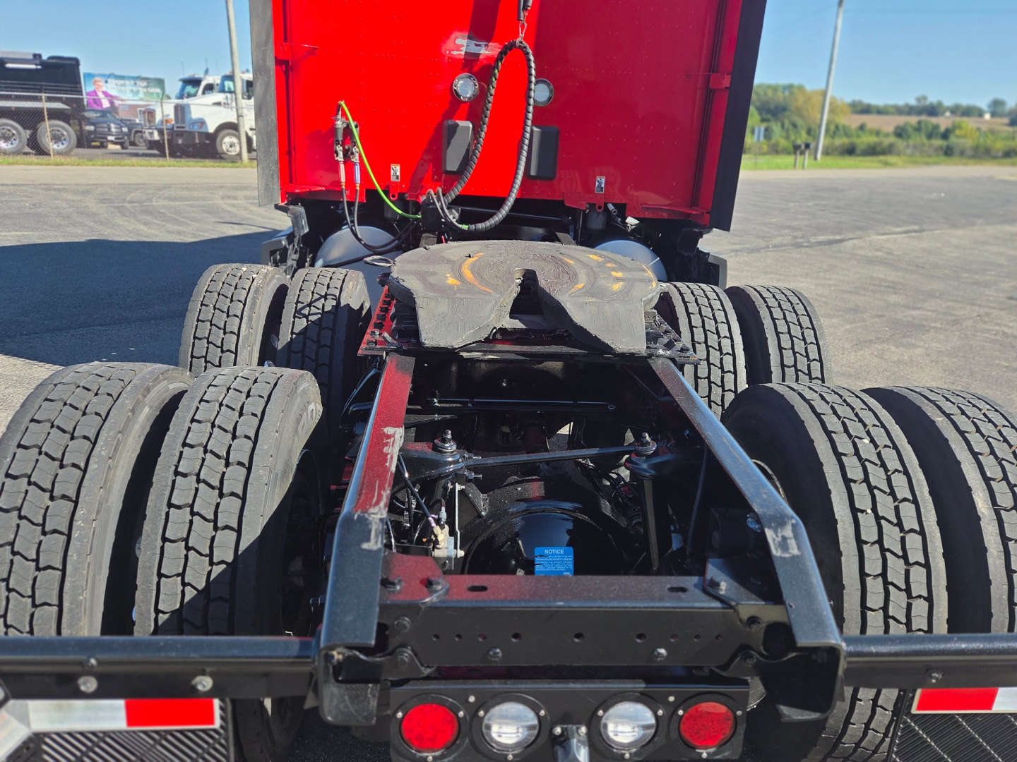 Kenworth T680 chassis rear view showing fifth wheel and dual rear axles with dual tires, red cab mount, visible fuel lines and components.