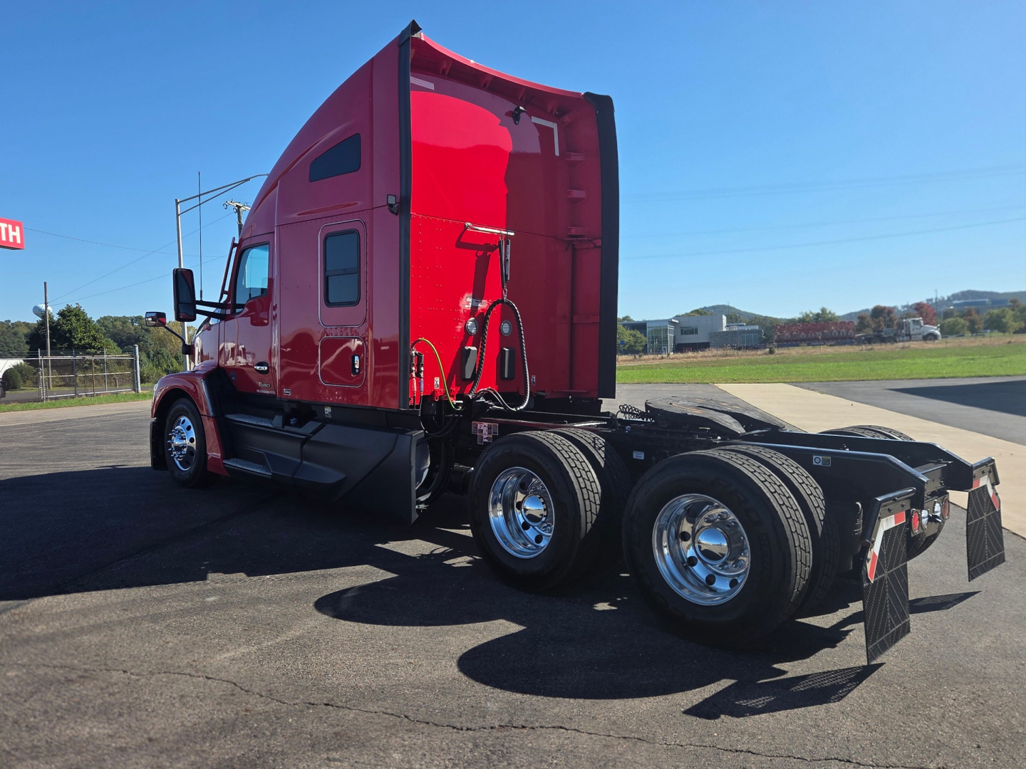 Kenworth T680 tractor semi-trailer chassis and red sleeper cab, side view showing rear dual axles and fifth wheel, with chrome wheels and black mud flaps.