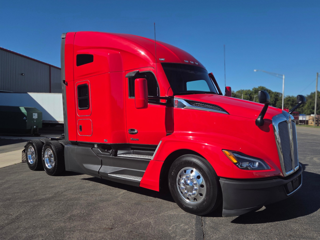 Kenworth T680 truck in red color, side view, sleeper cab, three rear axles visible, chrome wheels, daytime.