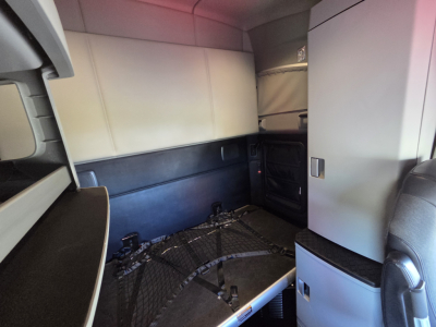 Kenworth T680 cab interior showing sleeper area with bunk space and storage cabinets, cargo restraint net, and seating visible.
