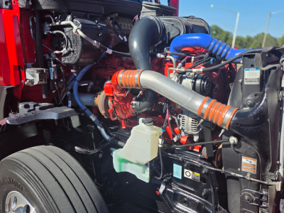 Kenworth T680 engine bay showing orange and blue hoses, coolant reservoir, and various engine components.
