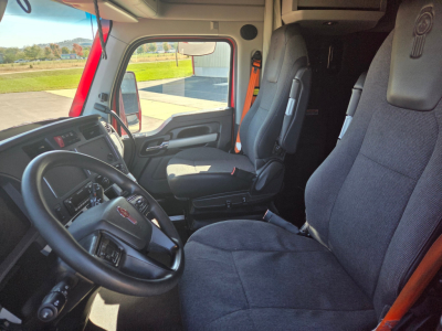 Kenworth T680 truck interior showing driver seat and front passenger seat, steering wheel, dashboard, and doorway; gray fabric seats and black steering wheel.