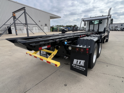 Rear view of a 2027 Mack GR64B roll-off truck showing the back platform and dual rear wheels.