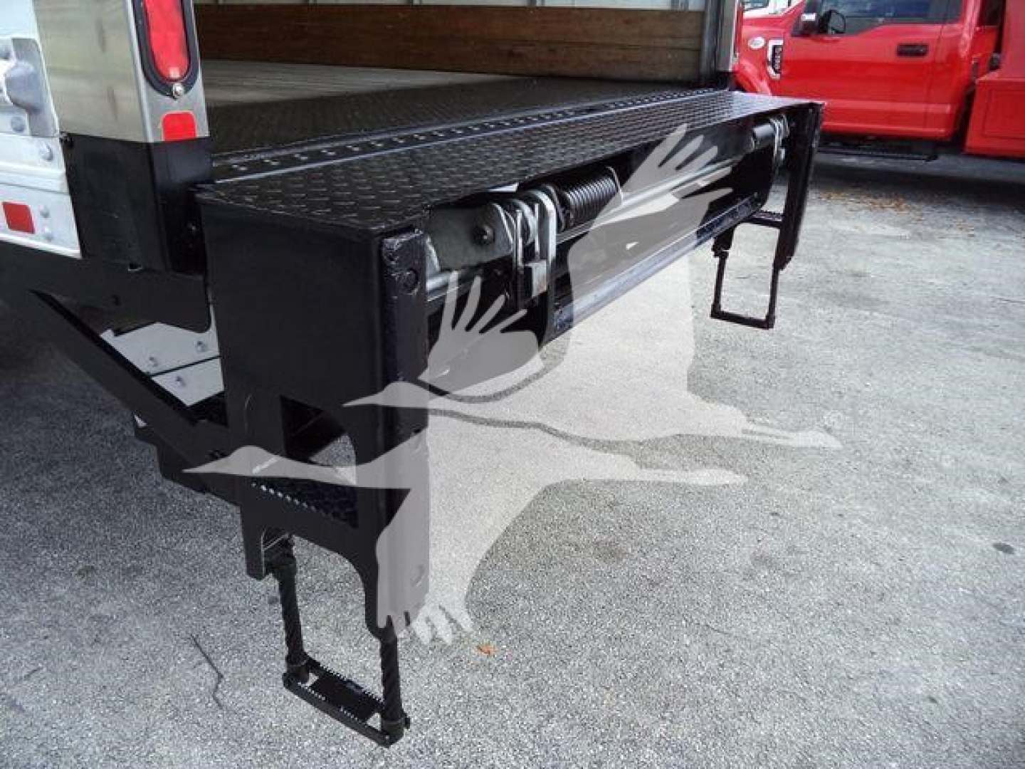 Truck bed with fold-down step and hydraulic tilt mechanism visible under the flatbed of a 2019 International 4300 truck.