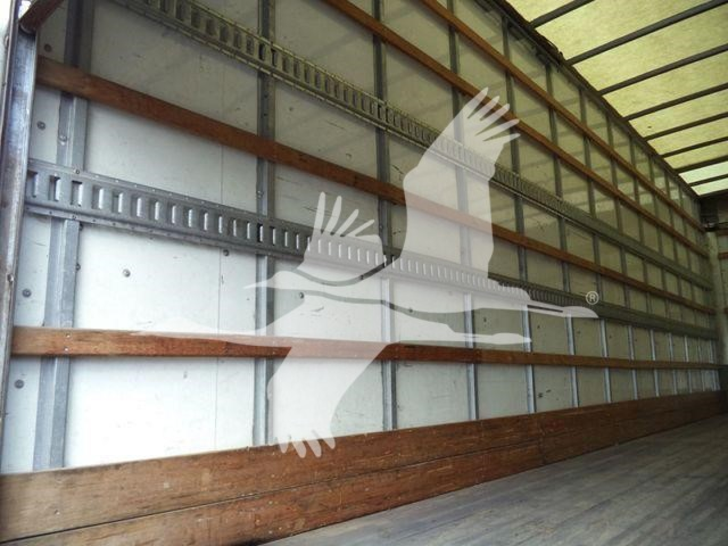 Interior of an empty transport trailer with metal walls and wooden floor; watermark of a soaring bird logo across the middle.
